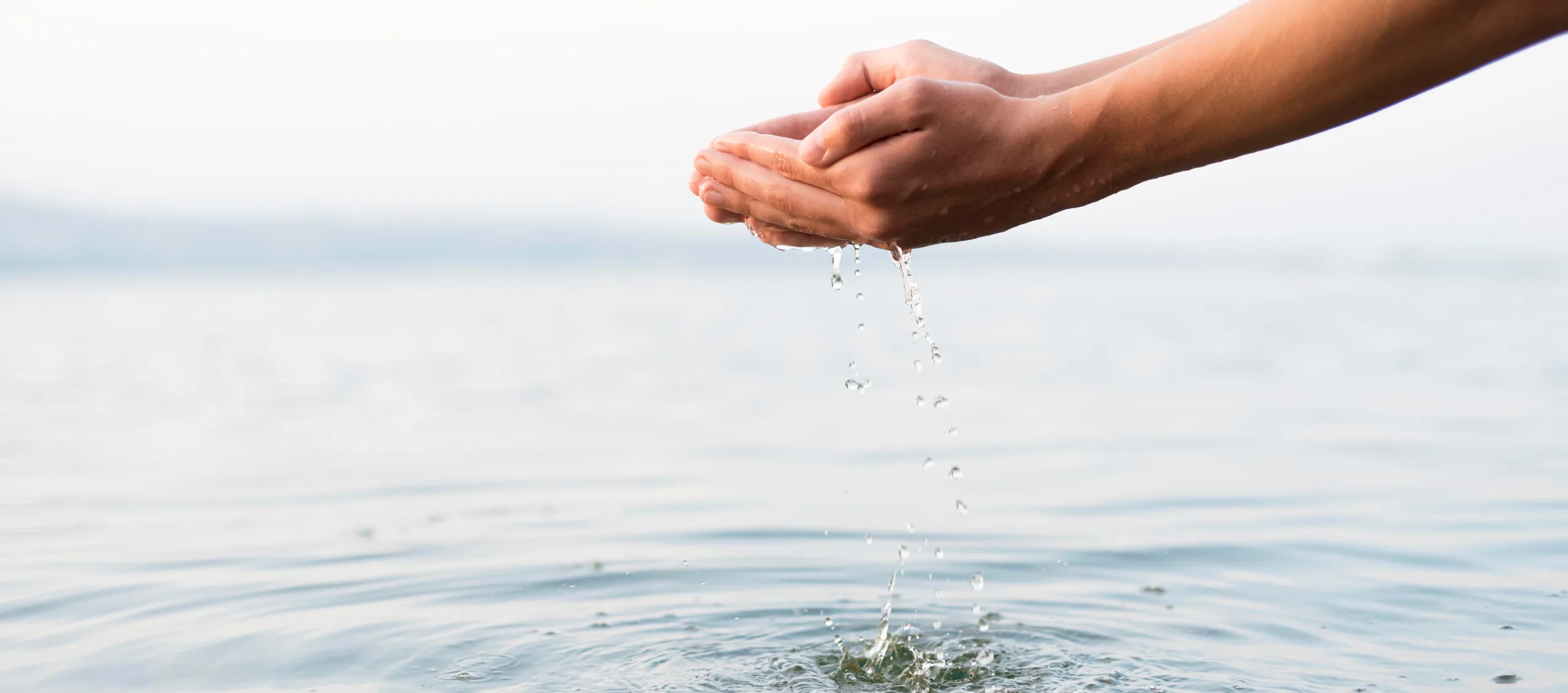 persona che prende dell'acqua con le mani in un lago